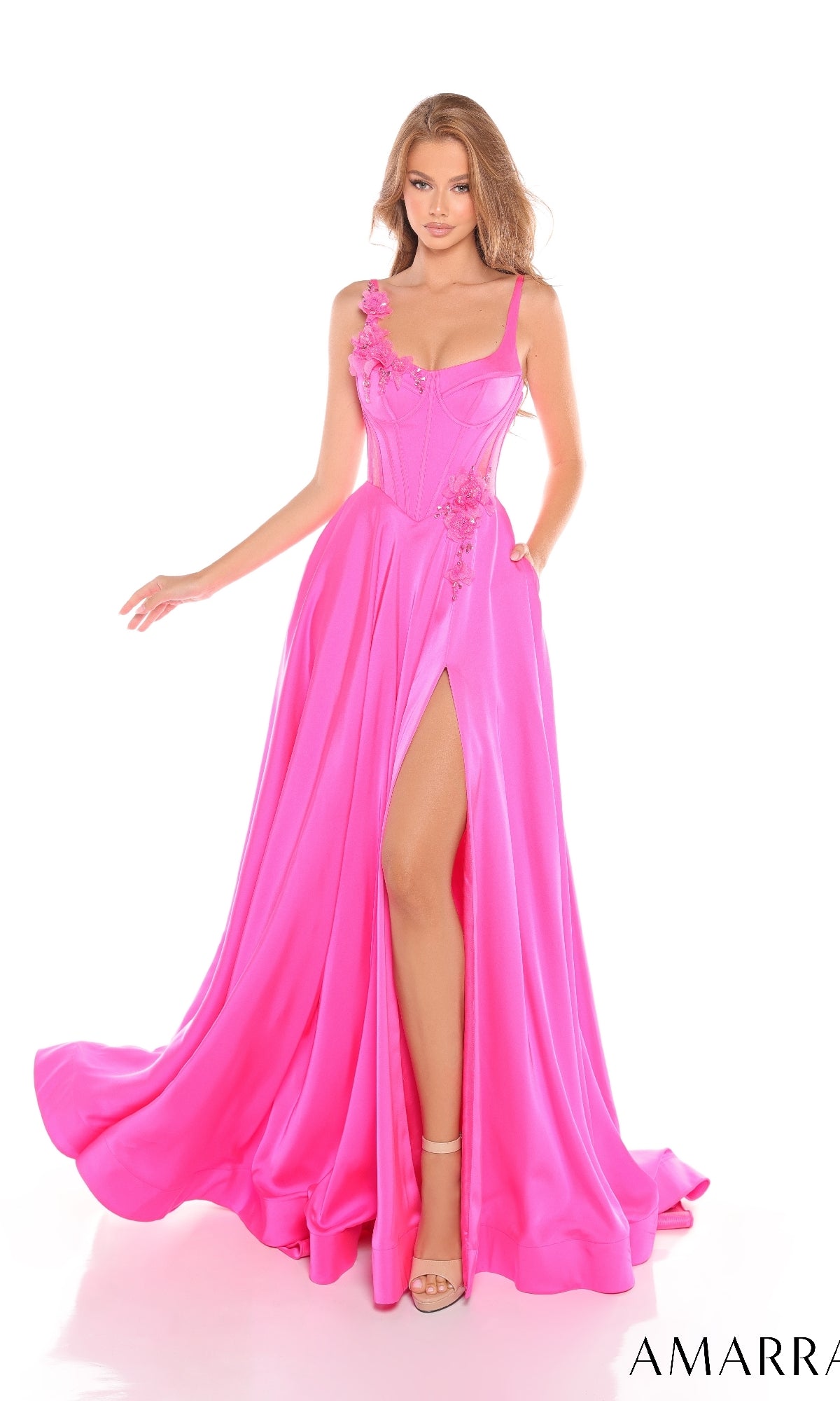 A woman poses against a white background wearing the Amarra 88214 long prom dress, featuring bright pink color, a corset bodice, floral details, and a high leg slit.